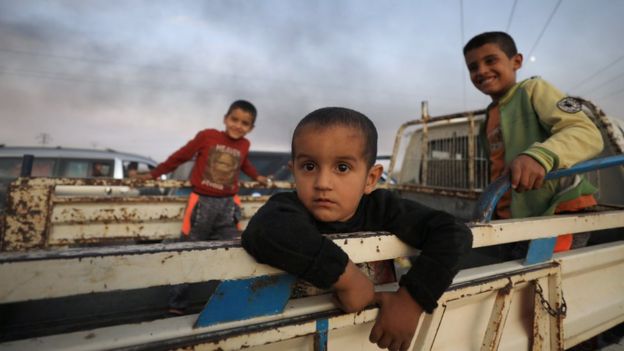 Boys stand at a back of a truck as they flee Ras al Ain town