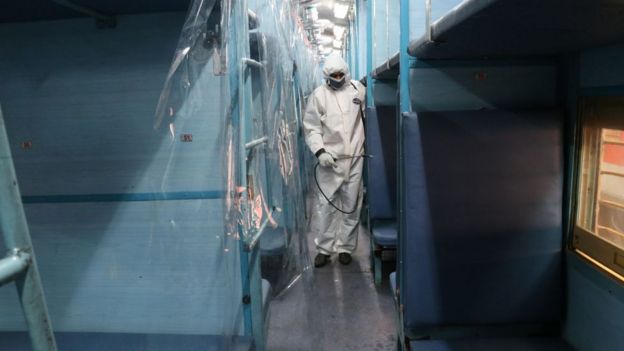 A worker in protective gear sprays disinfectant inside a train carriage converted into an isolation ward