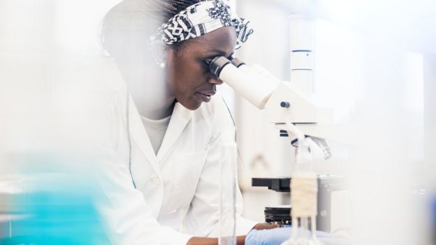 Pesquisadora olha por microscópio em laboratório
