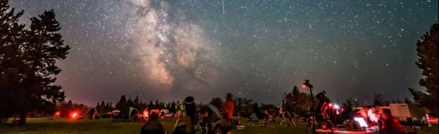 Un grupo de personas mirando las estrellas, el cielo está iluminado con meteoritos y la vía láctea.