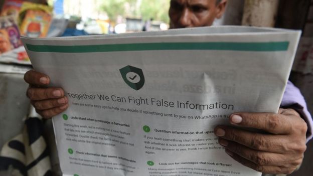 This photo illustration shows an Indian newspaper vendor reading a newspaper with a full back page advertisement from WhatsApp intended to counter fake information, in New Delhi on July 10, 2018