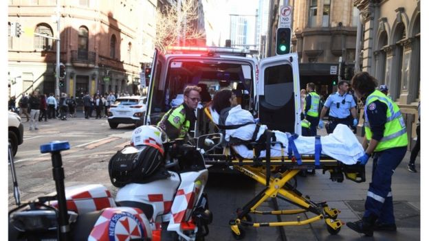 Emergency services helping a woman on a stretcher into an ambulance