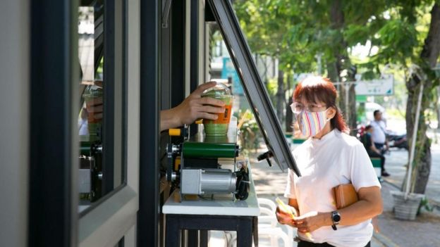 Uma mulher na Tailândia recebe sua bebida de um vendedor a uma distância segura, graças a uma esteira automática