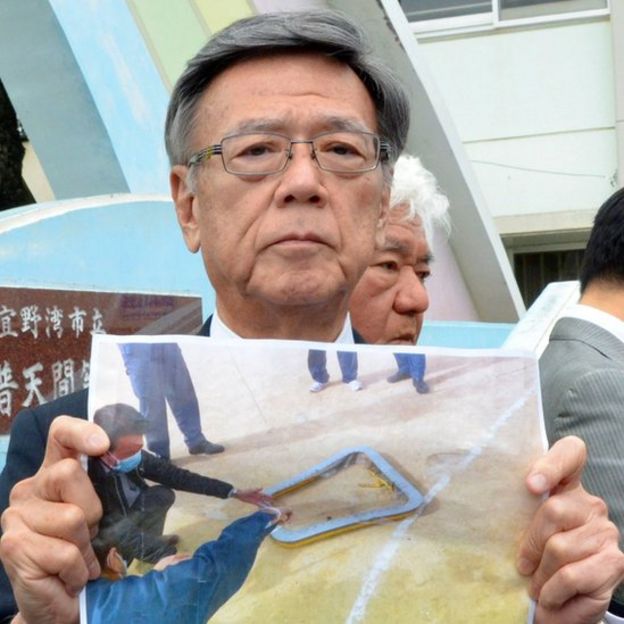 Il governatore di Okinawa Takeshi Onaga mostra una foto del vento caduto dall'elicottero