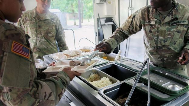 Un soldado sirviéndole comida a otro en un comedor militar