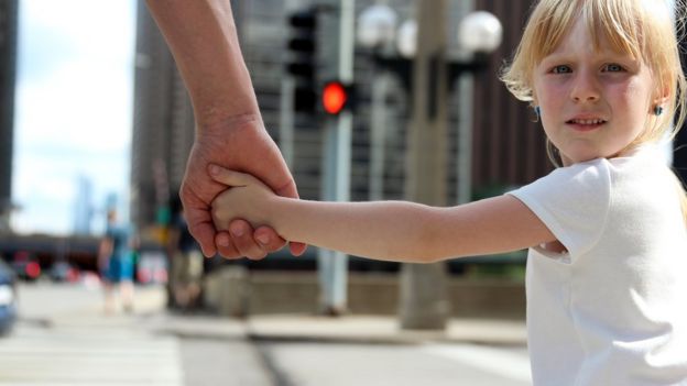 Niña en la calle de la mano de un adulto.