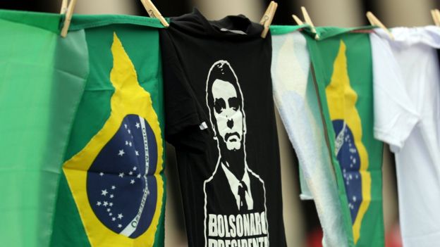 Camiseta de Bolsonaro pendurada em varal, ao lado de bandeiras do Brasil