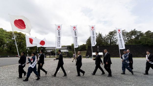 Hombres japoneses marchan con la bandera nacional cerca del palacio imperial.