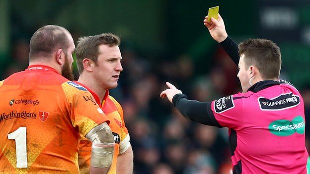 Referee Ben Whitehouse hands a yellow card to Scarlets prop Phil John