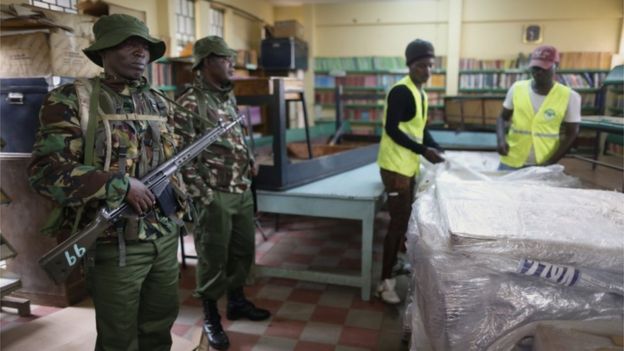 Electoral agents work to unpack electoral materials to be distributed to smaller polling stations, as police officers keep an eye on them at a tallying centre in the capital Nairobi, on 7 August 2017, a day before the country's general elections