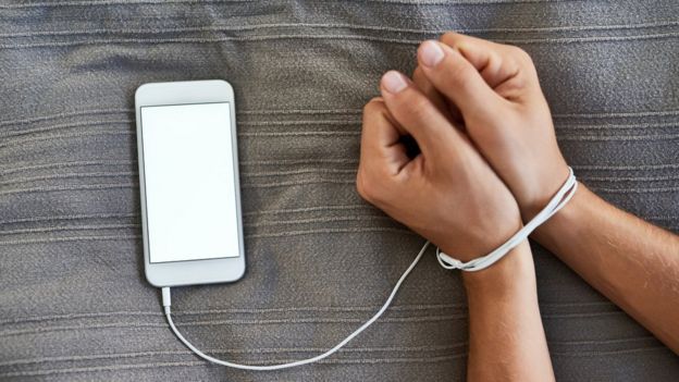 Unas manos atadas con el cable de un teléfono móvil