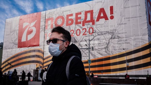 A man wearing a face mask, amid concerns of the COVID-19 coronavirus, walks in front of a huge banner for the upcoming 75th anniversary of the victory over Nazi Germany in World War II