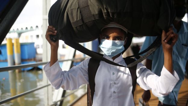 A boy wears a face mask and carries his luggage as he arrives by a ferry from his village to Dhaka at the Sadarghat Launch terminal after the lifting of the lockdown, Dhaka, Bangladesh 01 June 2020.