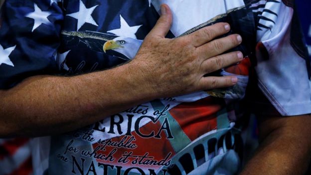 Seguidor de Trump con la mano en el corazón vistiendo una remera con la bandera de Estados Unidos y el águila.