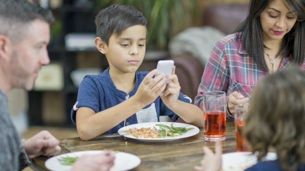 طفل ينظر إلى هاتفه أثناء تناول الطعام