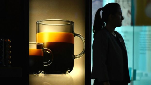 A woman stands alongside a promotional poster for Nespresso at the brand's Swiss headquarters in Vevey, 20 October 2016