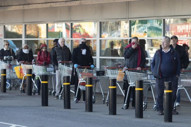 Clientes na fila do lado de fora de um supermercado.