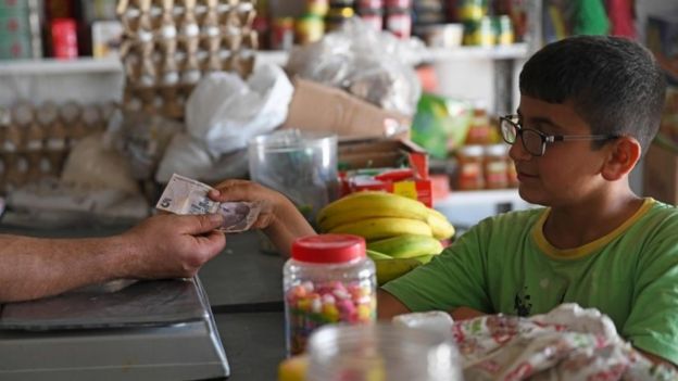 A boy uses Turkish lira to buy food at a shop in rebel-held Aleppo province, Syria (10 June 2020)