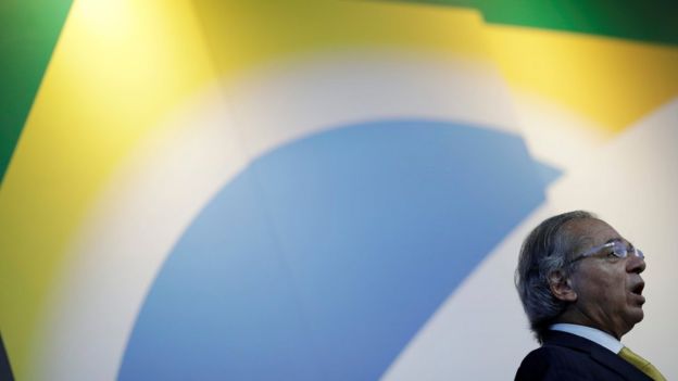O ministro da Economia, Paulo Guedes, aparece de perfil com uma bandeira do Brasil impressa ao fundo