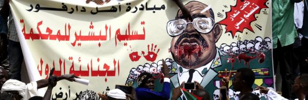 Sudanese protesters hold up a banner depicting ousted president Omar al-Bashir with text in Arabic reading: "Darfur people's initiative: handing over al-Bashir to the International Criminal Court (ICC)", in the capital Khartoum, 19 April 2019