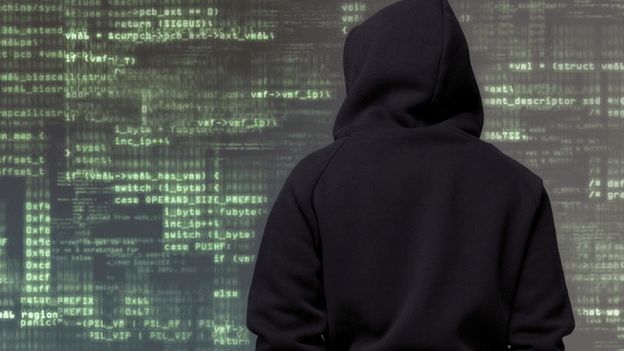 A man in a hood standing in front of code