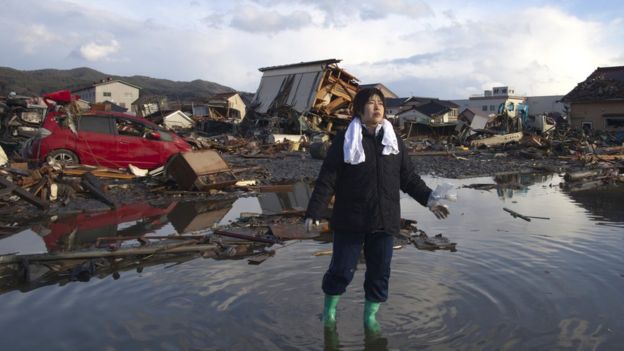 Una mujer de pie en el agua entre los destrozos causados por un tsunami