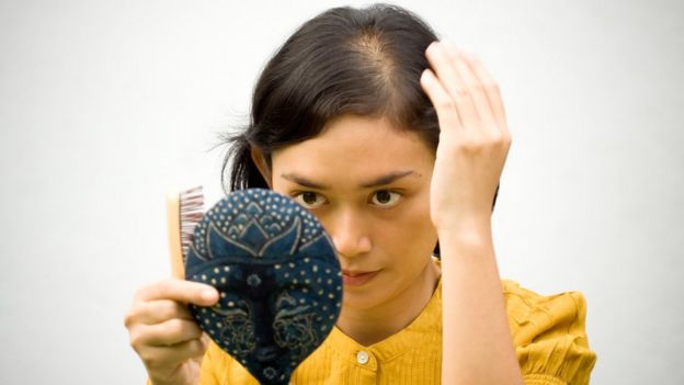 Mujer con principio de alopecia mirándose al espejo.