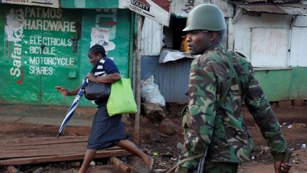 A woman runs in front of a policeman during clashes between opposition supporters and police in Kawangware slum in Nairobi (30 October 2017)