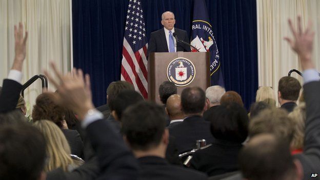 Director John Brennan, shown at the CIA's first live TV conference, answers questions at a podium
