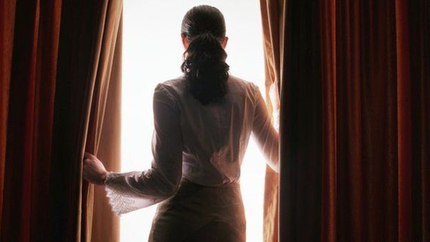 Woman looking through curtains