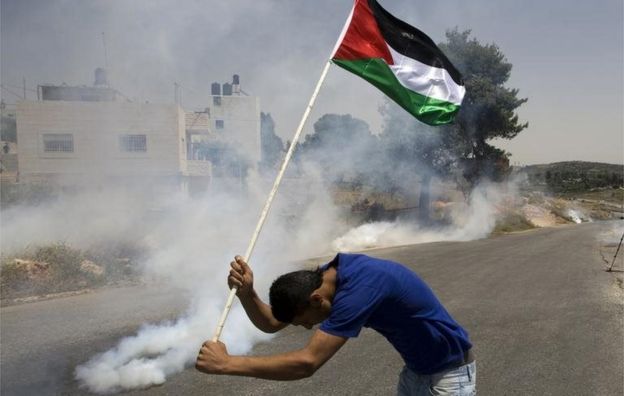 Un palestino sostiene su bandera entre gases en Nabi Saleh (foto de archivo)