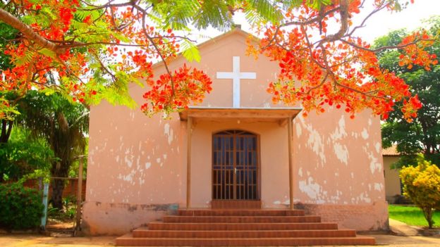 Igreja de Araguainha, pequena e pintada de cor de rosa, à frente de uma árvore florida com flores vermelhas