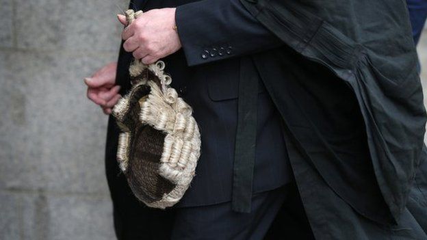 A barrister holds his wig as he arrives at The Old Bailey