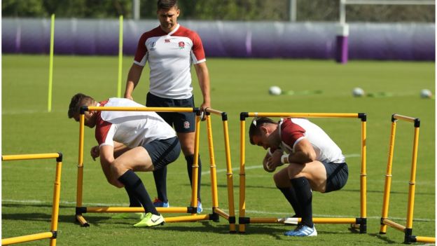 Owen Farrell (L) and team mate George Ford crouch under a hurdle watched by Ben Youngs during the England Rugby team training session