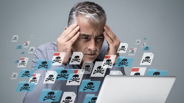 Hombre frente a pantalla de computadora que pareciera infectada de virus.