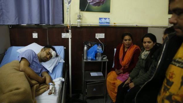 Basanta Bohora, who escaped the plane, sleeps in a hospital bed as family look on