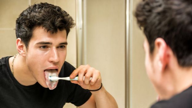 Hombre joven frente al espejo cepillándose la lengua.