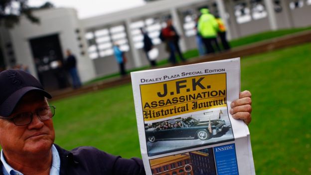 Turista segura jornal falando da morte de John Kennedy em frente à praça Dallas, nos EUA