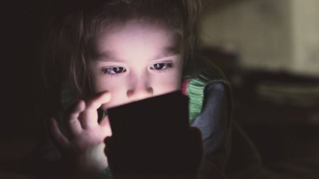 Niña viendo una pantalla a oscuras.