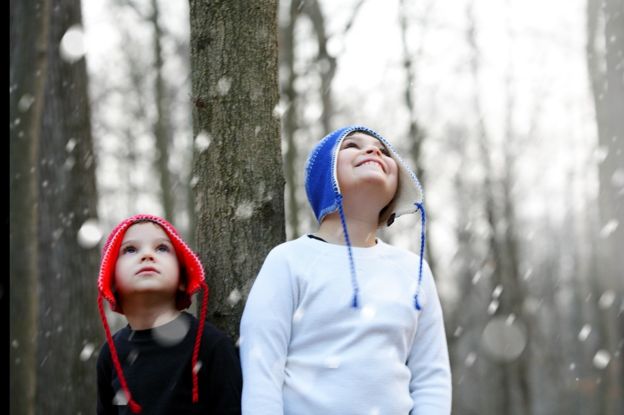 Dos niños en el bosque mientras nieva.