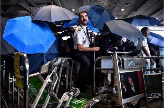 一名航空公司职员试图穿过示威者的人墙和雨伞阵。
