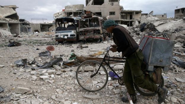 A Syrian man pushes his bike past destroyed buildings in the besieged rebel-held town of Douma on 30 March 2018