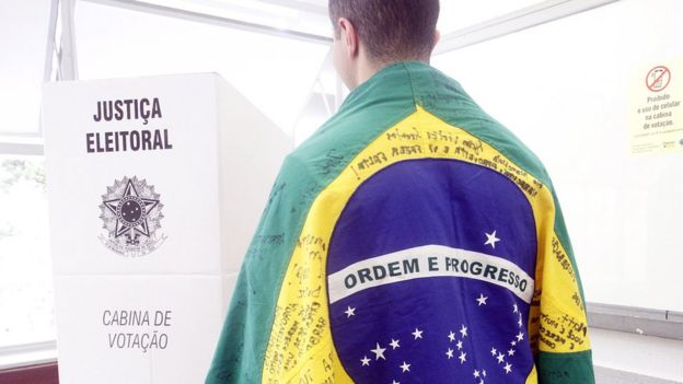 Homem envolvo em uma bandeira do Brasil se dirige à cabina de votação, em Belo Horizonte, Minas Gerais