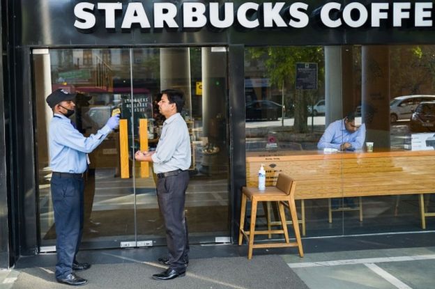 A security guard (L) takes the temperature of a patron as a preventive measure against the COVID-19 novel coronavirus before he enters a Starbucks coffee shop in New Delhi on March 17, 2020