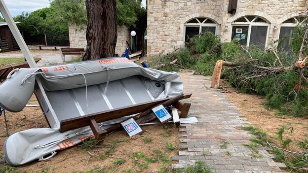 A life boat is photographed on is side, amidst broken trees