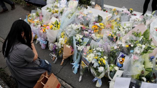 A woman prays in front of a row of flowers placed for victims of the torched Kyoto Animation building