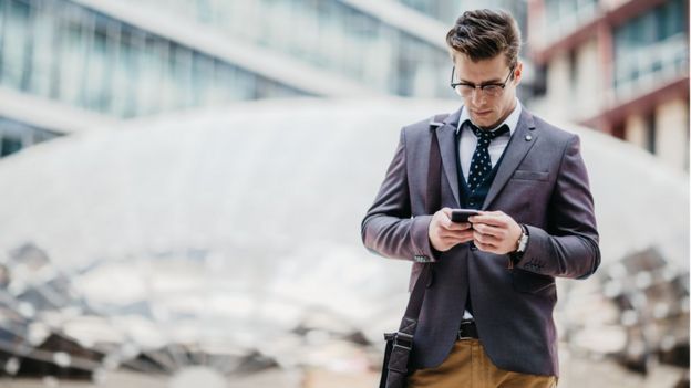 Un joven en traje mira su celular.