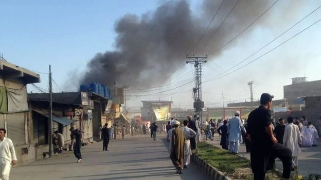 Residents gather along a road as smoke billows after a twin blasts at a market in Parachinar (23 June 2017)
