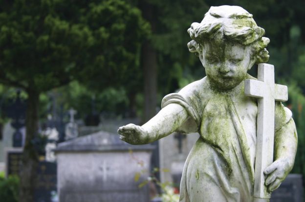 Stone statue of a child holding a cross in a cemetery