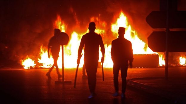 Lebanese protesters walk past burning tyres in the southern town of Sidon on 17 December 2019